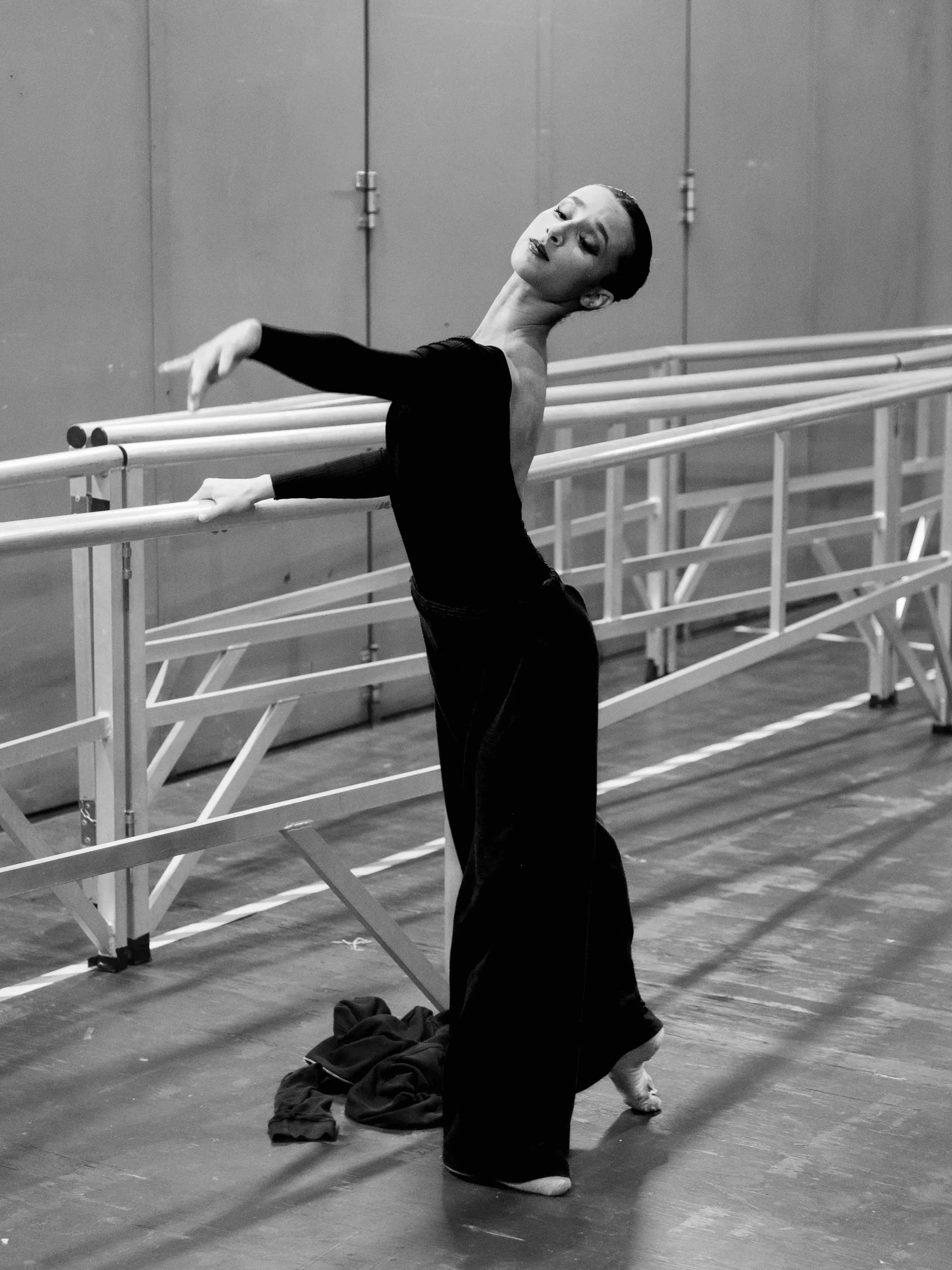 Una ballerina in nero si allunga alla sbarra dietro le quinte