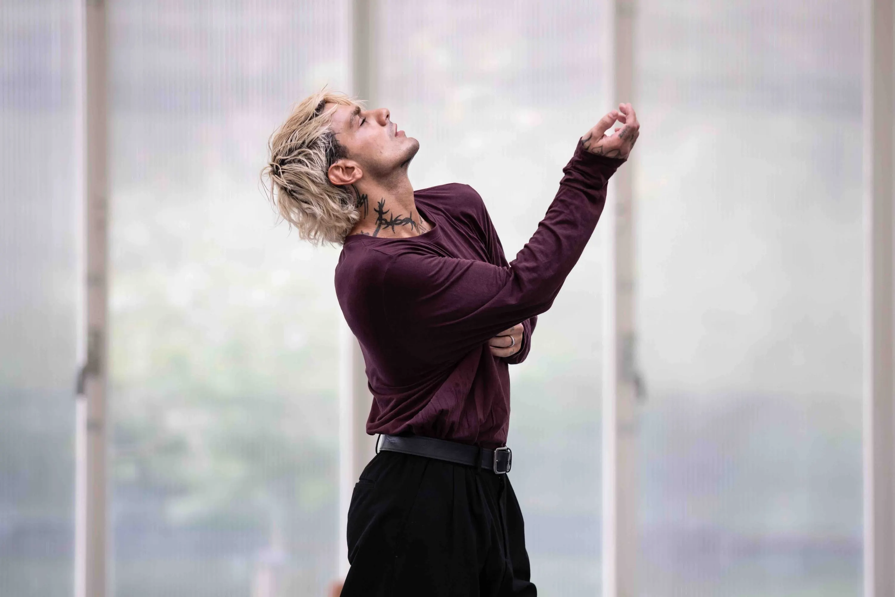 Un danzatore in rosso scuro con il braccio alzato davanti alla finestra