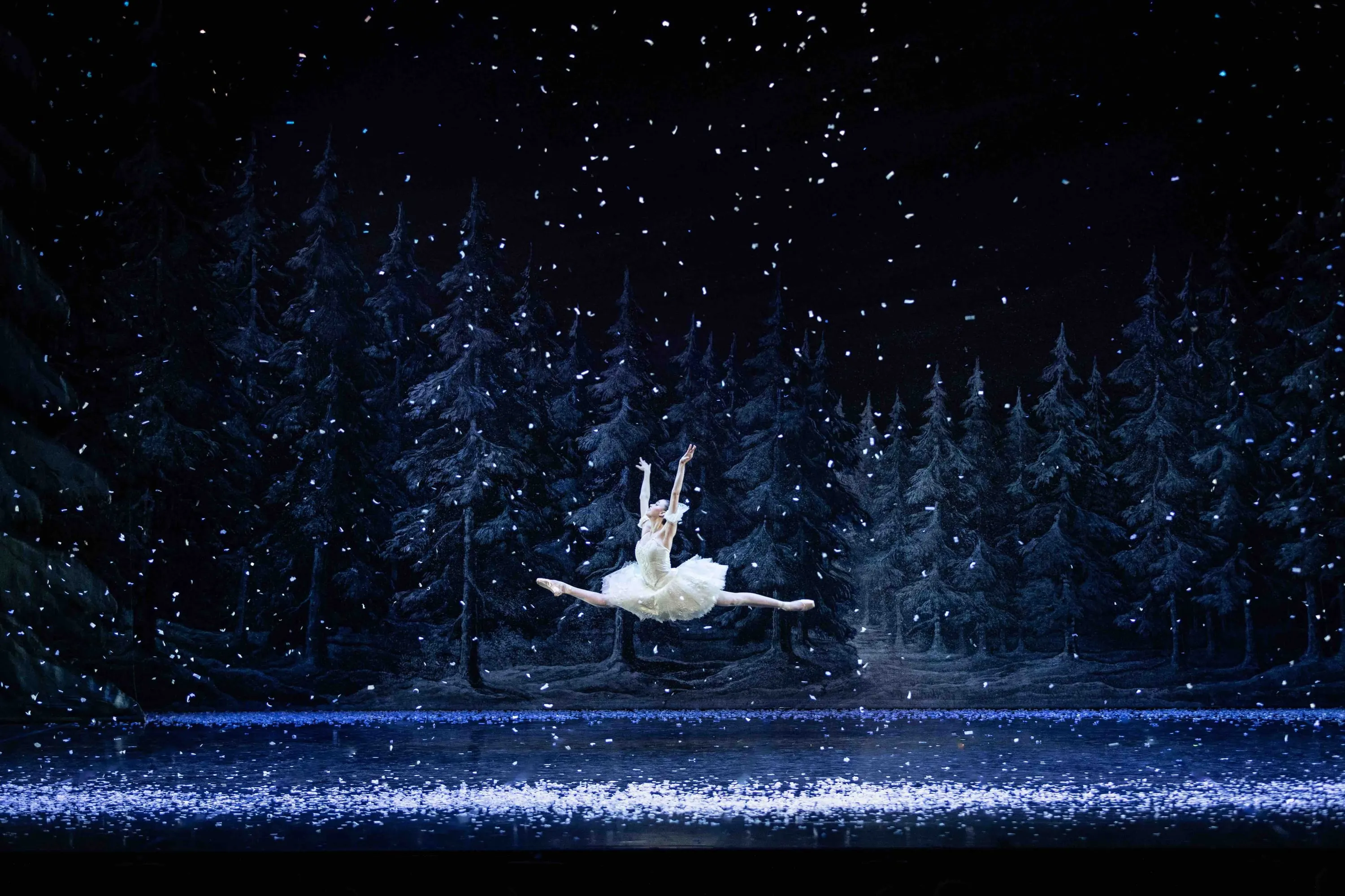 Una ballerina in salto nel bosco con la neve che cade