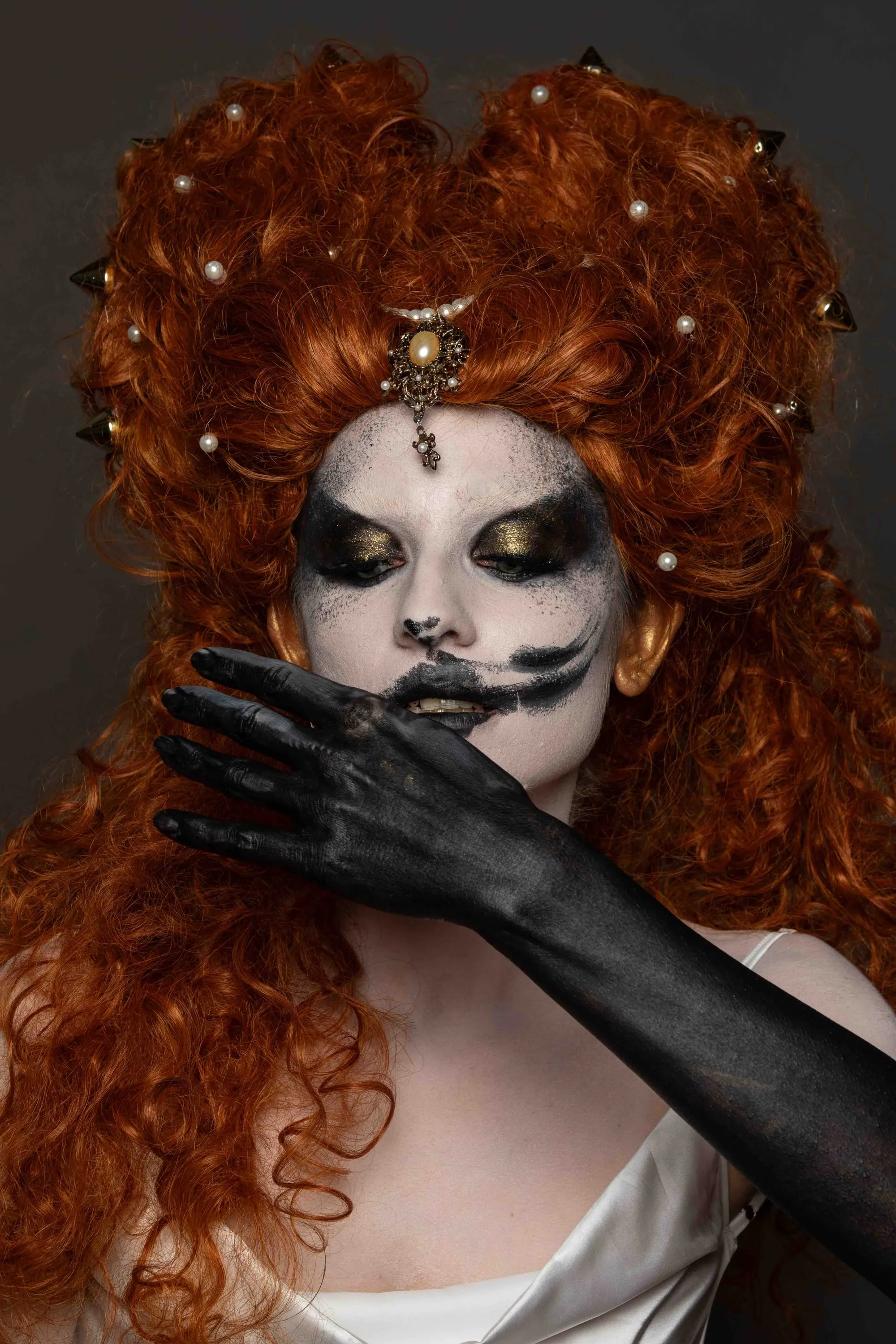 Parrucca rossa e trucco teatrale, una mano nera copre la bocca