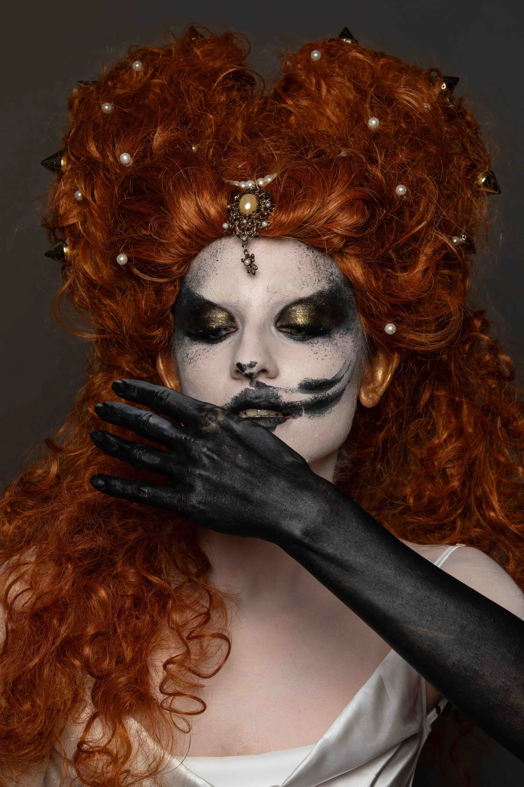 Parrucca rossa e trucco teatrale, una mano nera copre la bocca