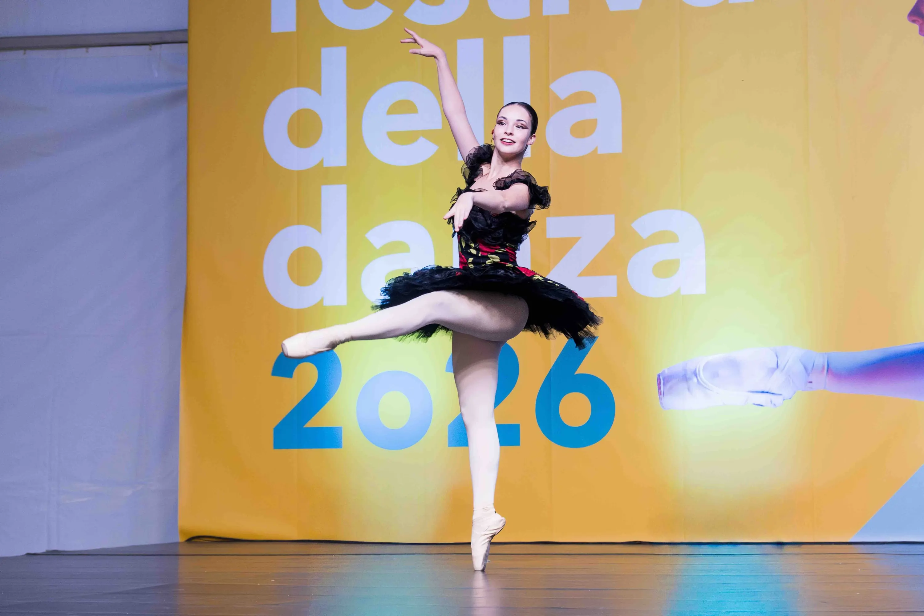 Ballerina in tutù nero in arabesque davanti al fondale giallo del festival