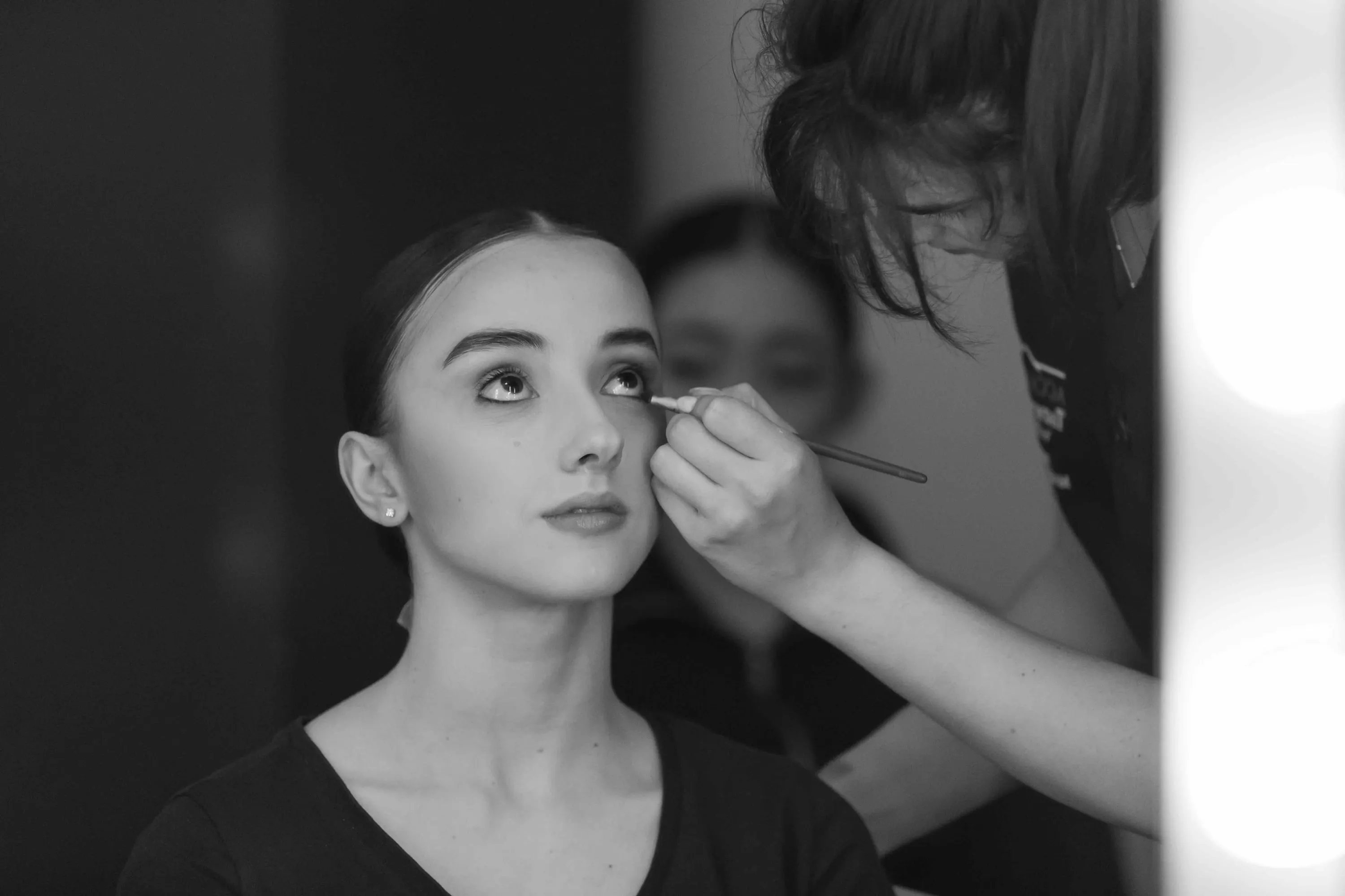 Una ballerina viene truccata, gli occhi rivolti in alto