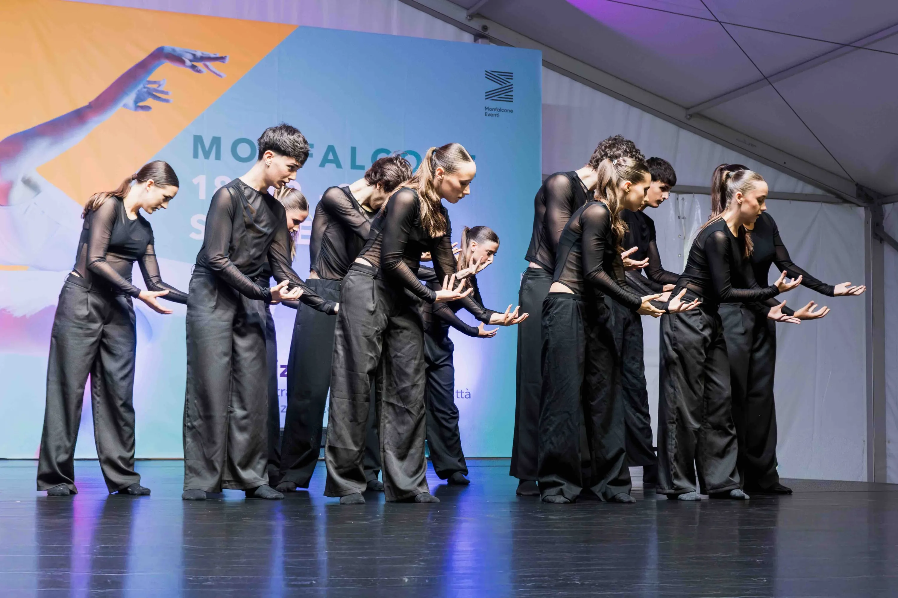 Fila di danzatori in nero con le braccia tese in avanti