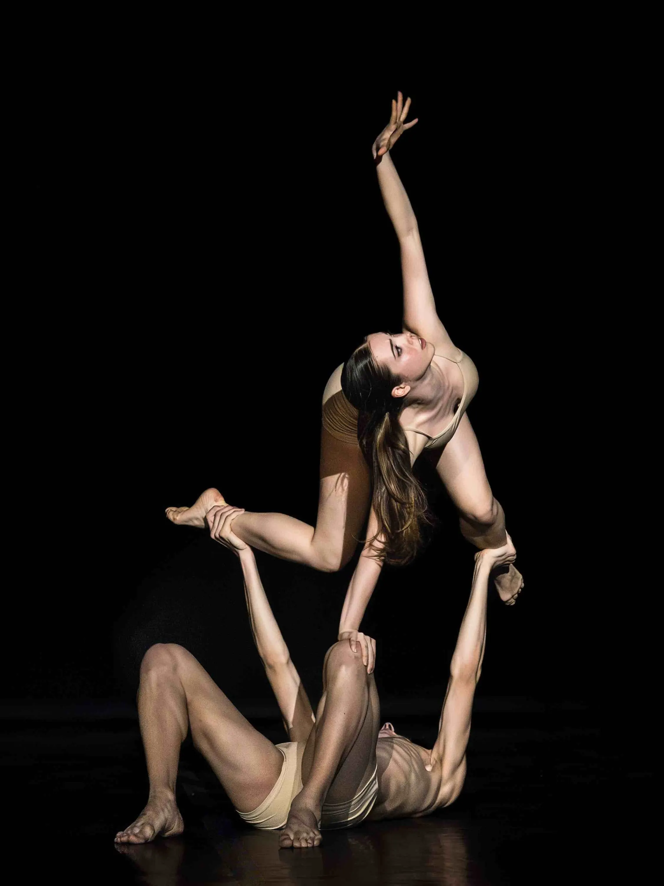 Una ballerina in equilibrio sopra il compagno sdraiato a terra, su fondo nero